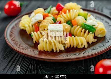 Pâtes Penne aux légumes, petits pois, poivrons, tomates, sauce, mozzarella sur fond de bois noir. Pâtes italiennes avec légumes et sp Banque D'Images