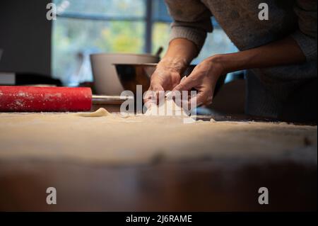 Vue à angle bas d'une femme qui étire soigneusement la pâte vegan maison pour strudel ou tarte sur une table à manger. Banque D'Images