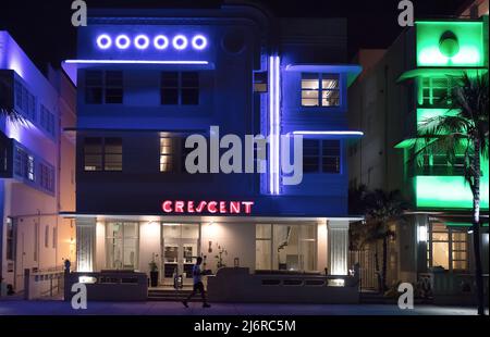 Un homme passe devant des bâtiments art déco éclairés aux néons sur South Beach, Miami, Floride, États-Unis Banque D'Images