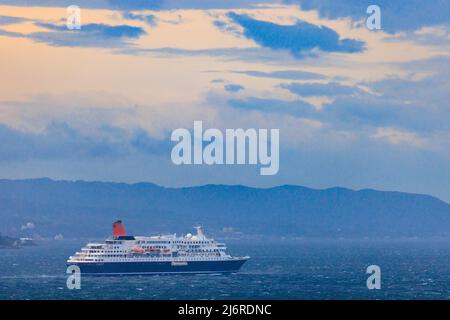 Croisière en ferry le long de la côte au coucher du soleil sous les nuages Banque D'Images