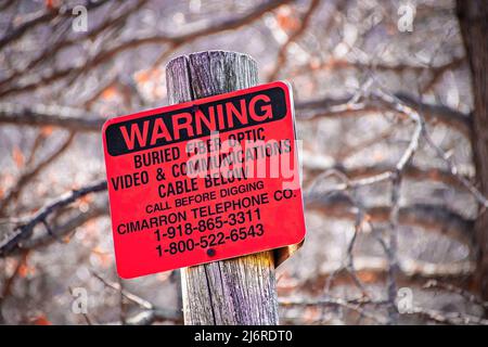 3-16-2022 Osage Co. OK USA - panneau rouge affiché sur le poteau lit avertissement câble en fibre optique enterré - arrière-plan bokeh des arbres d'hiver - gros plan Banque D'Images