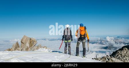 Couple cordage d'équipe connecté avec harnais d'escalade vêtements d'alpinisme habillés avec sacs à dos et haches de glace en profitant de la vue sur le Mont blanc (Mont Banque D'Images