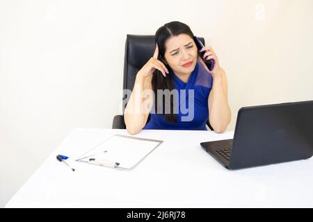 Beau assistant de PDG réussi, portant un chemisier bleu inquiet de maux de tête, sur un appel, bureau avec ordinateur portable, sur fond blanc Banque D'Images