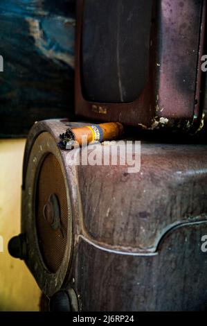 Le cigare Cohiba cubain fumé est laissé sur le dessus d'un ancien radio Shortwave décomposé Banque D'Images