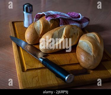 Petits pains de lait frais faits maison, pain savoureux, petits pains, tout sur une planche à découper, saupoudreuse, couteau de cuisine et tout dans une atmosphère de petit déjeuner. Banque D'Images