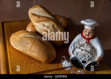 Du pain frais et savoureux, des petits pains, un couteau de cuisine avec un peu de farine sur une figure du cuisinier, le tout sur une planche à découper. Banque D'Images