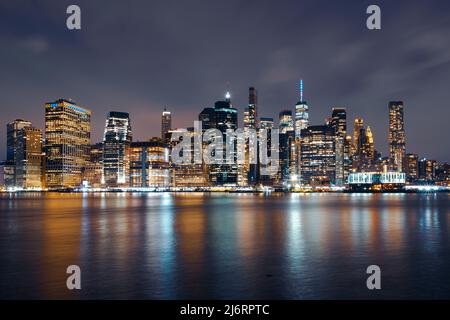 Manhattan Skyline la nuit avec des bâtiments illuminés en bleu et jaune pour soutenir l'Ukraine et coloré East River Banque D'Images