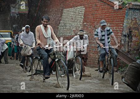 Des hommes qui négocient avec une route inondée lorsqu'ils sont à vélo pendant une journée de mousson à Varanasi, Uttar Pradesh, Inde. Banque D'Images