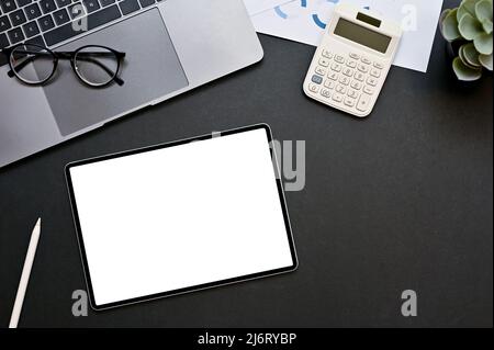 Vue de dessus de l'espace de travail professionnel avec ordinateur portable, lunettes, calculatrice, documents financiers et maquette d'écran blanc de tablette sur fond noir. Banque D'Images