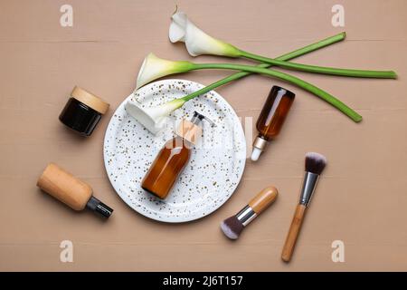 Composition avec produits cosmétiques, pinceaux de maquillage et nénuphars sur fond de bois de couleur Banque D'Images