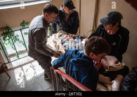 Des volontaires du centre informel d'aide humanitaire 'vvolunter68' évacuent Kiseleva Larisa Anatolyevna, 55 ans, qui a la sclérose en plaques, de son appartement dans le quartier fortement bombardé de Saltivka à la gare de Kharkiv, où elle prendra le train pour Lviv puis se rendra en Pologne. La Russie a envahi l'Ukraine le 24 février 2022, déclenchant la plus grande attaque militaire en Europe depuis la Seconde Guerre mondiale Banque D'Images