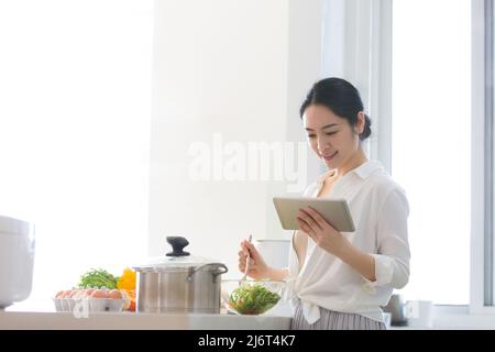 Jeune femme au foyer utilisant une tablette pour prendre des cours de cuisine dans la cuisine familiale - photo de stock Banque D'Images