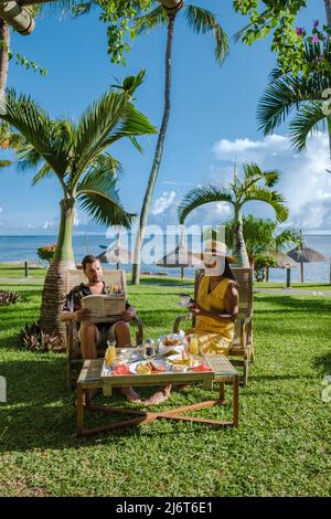 couple d'hommes et de femmes de milieu d'âge prenant le petit déjeuner dans un jardin tropical avec des palmiers. Banque D'Images