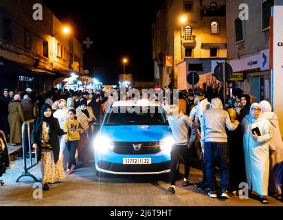 Taxi bleu nuit passant dans les rues bondées de l'avenue Mohamed Zerktouni, Essaouira pendant les célébrations du Ramadan Banque D'Images