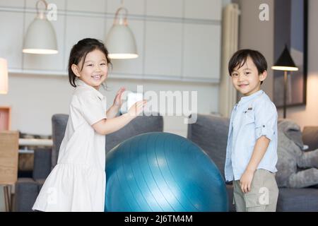 Une petite fille et un petit garçon jouant intimement sur la balle d'exercice dans le salon - photo de stock Banque D'Images
