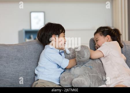 Une petite fille et un petit garçon jouent avec joie avec une poupée d'éléphant farcie sur le canapé du salon - photo de stock Banque D'Images