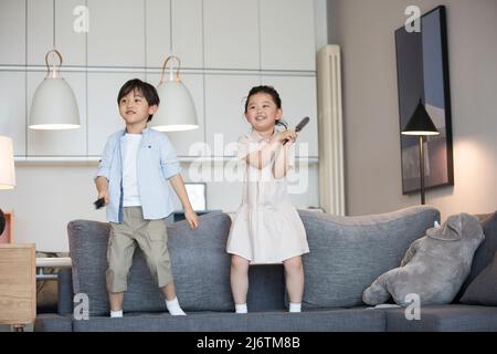 Une petite fille et un petit garçon chantant sur le canapé avec un peigne agissant comme un microphone - photo de stock Banque D'Images