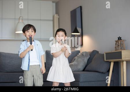 Une petite fille et un petit garçon chantant avec un peigne comme microphone dans le salon - photo de stock Banque D'Images