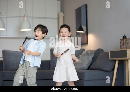 Une petite fille et un petit garçon chantant avec un peigne comme microphone dans le salon - photo de stock Banque D'Images