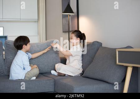 Une petite fille et un petit garçon jouent main clapping sur le canapé du salon - photo de stock Banque D'Images