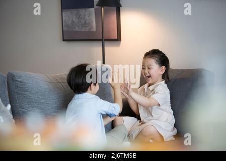 Une petite fille et un petit garçon jouent main clapping sur le canapé du salon - photo de stock Banque D'Images