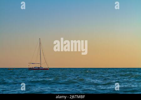 Un petit voilier flotte dans la mer au coucher du soleil Banque D'Images