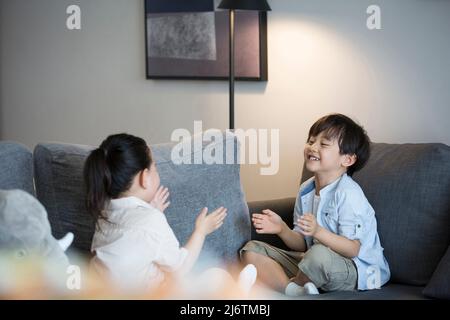 Une petite fille et un petit garçon jouent main clapping sur le canapé du salon - photo de stock Banque D'Images