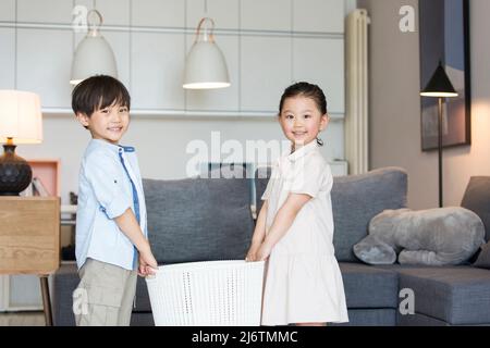 Près du canapé du salon, les frères et sœurs portent un panier blanc ensemble - photo de stock Banque D'Images