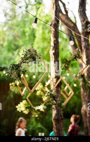 Réception de mariage à l'extérieur dans la forêt de pins. Tables à manger, bancs décorés dans le style boho avec bougies, fleurs, lumières de fée printanière, assiettes Banque D'Images