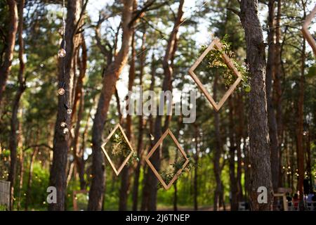 Réception de mariage à l'extérieur dans la forêt de pins. Tables à manger, bancs décorés dans le style boho avec bougies, fleurs, lumières de fée printanière, assiettes Banque D'Images
