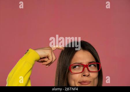 demi-portrait d'une jeune femme avec des lunettes se grattant la tête sur fond rose Banque D'Images