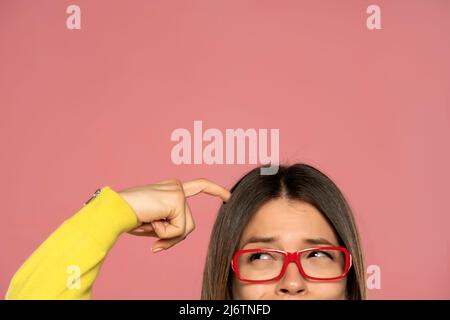 demi-portrait d'une jeune femme avec des lunettes de vue se grattant la tête sur un fond blanc Banque D'Images