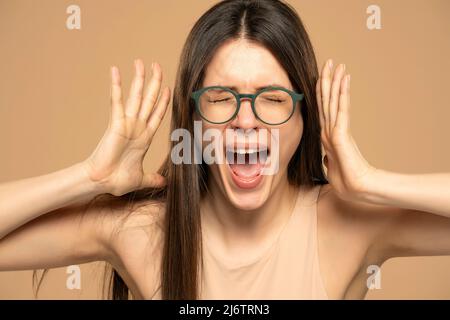 Gros plan portrait stressé femme frustrée avec des lunettes criant ayant temper tantrum isolé sur fond beige. Négatif humain émotion faciale ex Banque D'Images