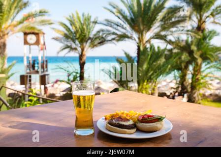 Un verre de bière et un hamburger sur une table en bois contre la mer Banque D'Images