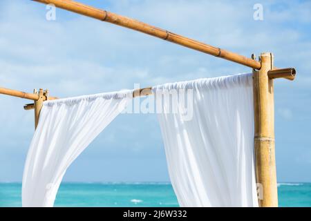 Un fragment de belvédère vide avec des rideaux blancs sur un cadre en bambou se trouve sur une plage de sable, République dominicaine, plage de Bavaro Banque D'Images