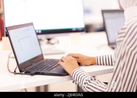 Fille musulmane afro-américaine avec hijab travaillant sur un ordinateur portable dans un bureau moderne. Banque D'Images