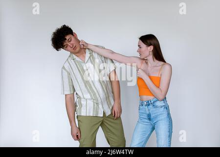 Portrait d'un jeune couple posé sur fond blanc. Jeune femme mécontente de poinçonner un homme évanoui avec les yeux fermés. Banque D'Images
