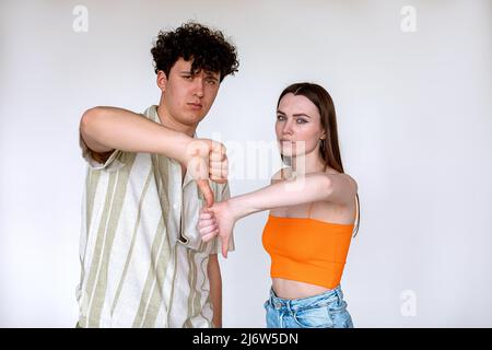 Portrait de jeunes couples mécontents posant sur fond blanc. Jeune contrarié malheureux homme, femme montrant le pouce vers le bas signe. Banque D'Images