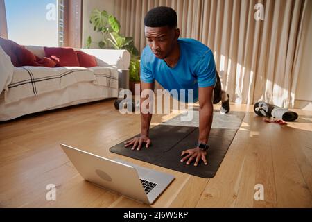 Jeune Afro-américain Noir en bonne santé homme travaillant à la maison avec une classe en ligne sur son portable tenant position de plan. Maintien de la forme Banque D'Images