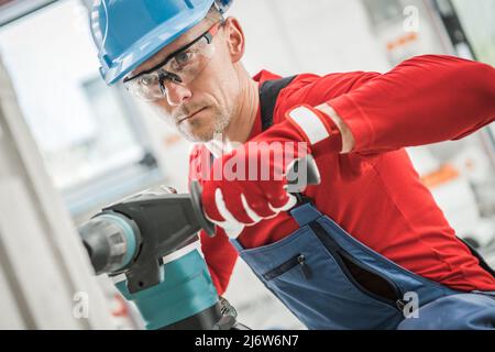 Entrepreneur en construction professionnel percer un autre trou pour un point de sortie électrique. Travailleur caucasien portant un casque et des lunettes de sécurité, Banque D'Images