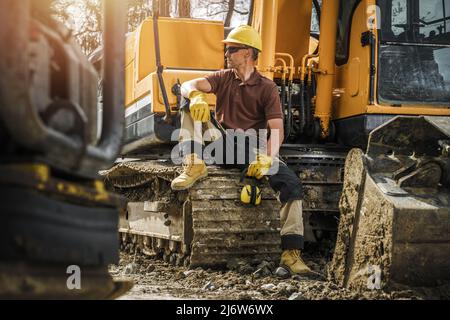 Construction professionnelle opérateur d'équipement de bouteur à chenilles dans son 30s prenant une courte pause déjeuner et profitant de la lumière chaude du soleil de printemps. Industrie de la construction et Banque D'Images