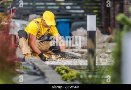 Travailleur de l'aménagement paysager caucasien dans son jardin d'arrière-cour du bâtiment de 40s Granite Bricks Path. Industrie résidentielle de l'aménagement paysager. Banque D'Images