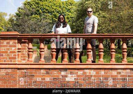 Femme asiatique et son petit ami blanc appréciant le soleil de printemps avec leur pedigree chocolat coolé chiot coloré Banque D'Images