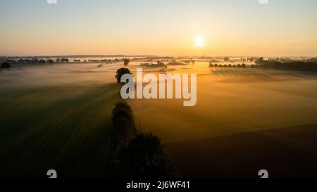 Lever de soleil spectaculaire en été. Panorama paysage brumeux. Matin brumeux, vue aérienne sur les champs verts et les prairies. Asphalte rural route vide. Drone agricole Banque D'Images