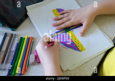 La fille dessine une photo dans l'album avec des stylos feutre. Stylos-feutres et tablette sur la table près de l'enfant Banque D'Images