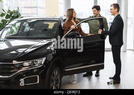 Un jeune couple méchant parle d'acheter une nouvelle voiture avec un vendeur d'automobiles chez un concessionnaire de véhicules Banque D'Images