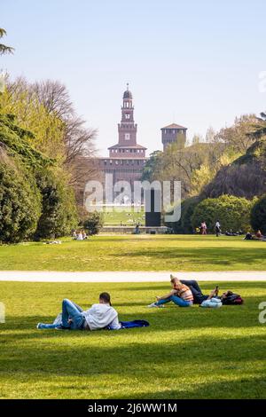 Les gens apprécient la pelouse du Parco Sempione (parc du Simplon) à Milan, en Italie, avec une vue sur les tours du Castello Sforzesco (château de Sforza). Banque D'Images