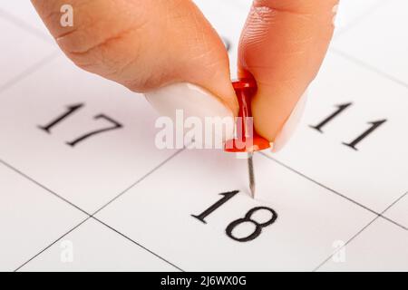 Épinglette rouge collée le jour du mois dans le calendrier, concept d'affaires. Belles mains de femmes Banque D'Images