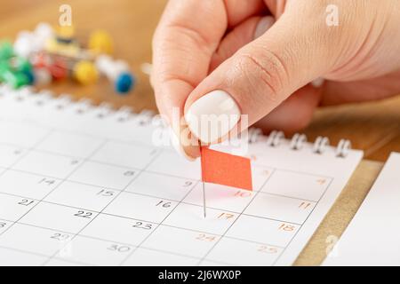 Les mains corrigeant l'horaire des notes, la vignette du drapeau rouge dans le calendrier pour la réunion et le rappel de rendez-vous Banque D'Images