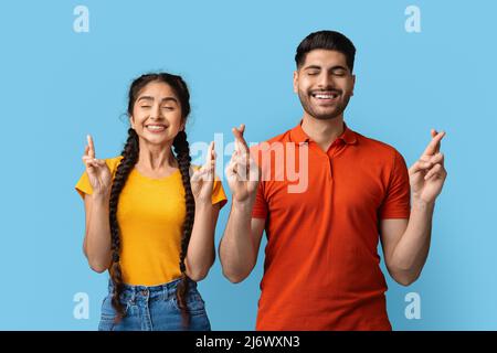 Joyeux couple moyen-oriental croiser les doigts pour faire Un souhait Banque D'Images